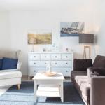 Wohnzimmer mit Sofa, Sessel, Tisch und Wandbildern.