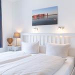 Schlafzimmer mit weißem Bett, zwei Nachttischen und Wandbild.