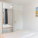 Schlafzimmer mit Bett, Spiegeltür und Wandbild mit Strandmotiv.