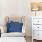 Ein Sessel mit blauen Kissen steht neben einem weißen Schrank.