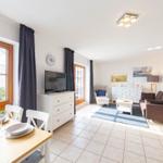 Wohn- und Essbereich mit TV, Sofa und Tisch. Fenster mit Vorhängen.