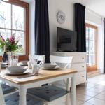 Essbereich mit Tisch, Stühlen und TV. Fenster mit dunklen Vorhängen.