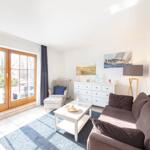 Wohnzimmer mit Sofa, Sessel, Tisch und Fenster zur Terrasse.