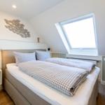 Schlafzimmer mit Dachschrägen, Dachfenster und Bett mit kariertem Bettzeug.