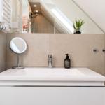 Badezimmer mit Waschtisch, Spiegel und Dusche unter Dachschräge.