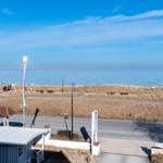 Meerfront mit Weg, Strand und kleinem Gebäude im Vordergrund.