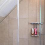 Dusche mit Glaswand, Duschbrause und Fliesen an geneigtem Dach