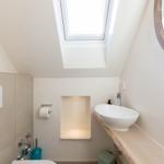 Badezimmer mit Dachschrägen, Waschbecken auf Holz, Spiegel und Dachfenster.