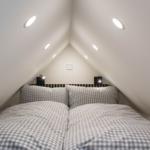 Doppelbett unter Dachschräge mit Nachttischlampen und eingebauten Deckenleuchten.