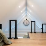 Dachgeschoss mit Holzboden, Wanduhr und schwarzen Ständern.