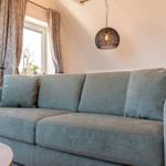 Ein grauer Sofa mit Kissen unter einer Pendellampe und Fenstern mit Vorhängen.