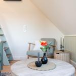 Wohnzimmer mit Sitzgelegenheiten und Holztreppe unter Dachschräge.