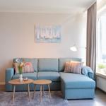 Ein Wohnzimmer mit blauem Sofa, zwei runden Tischen und einem Fenster mit Blick auf Balkon.