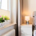 Schlafzimmer mit Bett, Nachttisch und Pflanze am Fenster.