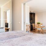 Zwei Betten mit gemusterten Bettwäsche. Im Hintergrund ist Esszimmer mit Holztisch und Stühlen.