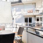 Terrasse mit Tisch und Stühlen, Sonnenschutz und Blick auf Balkon mit Möbeln.