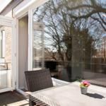 Terrasse mit Tisch, Stühlen und Pflanze. Durchgehende Glastüren führen ins Haus.