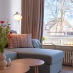 Wohnzimmer mit Sofa, Tisch und Blumen. Blick auf Balkon mit Pflanzen und Baum.