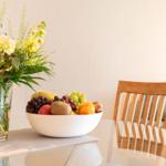 Auf dem Tisch steht eine Schale mit Obst und eine Vase mit Blumen.