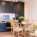 Küche mit Essbereich und Sofa. Holzstühle, Glasplatte, Blumen und Obst.