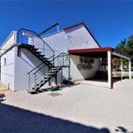 Weiße Villa mit Außentreppe und Carport. Fahrräder an Wand befestigt.