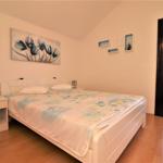 Schlafzimmer mit weißem Bett, Holzboden und Fenster mit Jalousie.