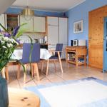 Essbereich mit Tisch, Stühlen und Küchenzeile. Blaue Wände, Holzmöbel und Blumen.