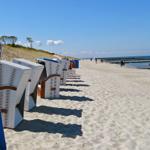 Strandkörbe stehen auf weißem Sand, Meer und Himmel sind blau.