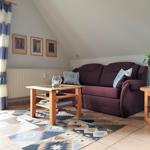 Wohnzimmer mit Sofa, Holztisch und Teppich. Fenster mit Vorhängen und Bilder an der Wand.