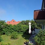 Hinterhof mit Grasfläche, Blumen und geschlossenem Sonnenschirm. Balkon und umliegende Bäume sichtbar.