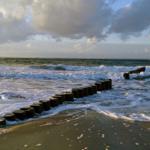 Strand mit Wellen und Holzpfosten entlang des Wassers.