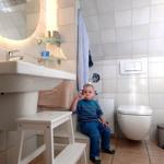 Badezimmer mit Waschbecken, Toilette und Kindersitzstuhl.