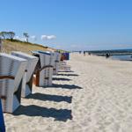 Strandkörbe stehen am Strand, im Hintergrund das Meer und Dünen.