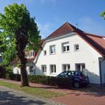 Weißes Haus mit rotem Dach, umgeben von Bäumen und einem gepflasterten Weg.