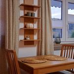 Holztisch mit zwei Stühlen, Wandregal und Fenster mit Blick auf Landschaft.