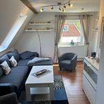 Wohnraum mit Sofa, Sessel und Fenster. Holzdielen und Dachschräge.