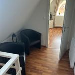 Zimmer mit Holzboden, schwarzen Sesseln und Blick in einen angrenzenden Raum.
