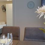 Esstisch mit Gläsern und Blumen, Blick in Schlafzimmer mit Bett und TV.