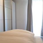 Schlafzimmer mit Bett, Kleiderschrank und Fenster mit Vorhängen.