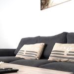 Grauer Sofa mit Kissen und Tisch mit Blumen und Fernbedienung.
