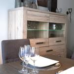Esstisch mit Gläsern und Blumen vor einem Sideboard.