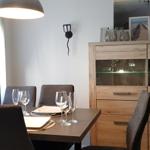 Esszimmer mit Tisch, Stühlen und Glasvitrine. Fenster mit Vorhängen und Wandbeleuchtung.