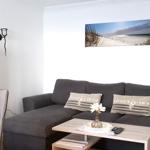 Wohnzimmer mit grauem Sofa, Holztisch und Wandbild von Strand.