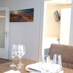 Essbereich mit Tisch, Stühlen und Gläsern. Hintergrund zeigt Schlafzimmer und Flur.