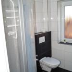 Badezimmer mit Dusche, WC und Fenster mit Pflanze.