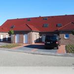Ferienhaus mit rotem Ziegeldach, mehreren Fenstern und Parkplätzen vorne.