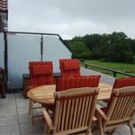Terrasse mit Holztisch und roten Sitzkissen. Blick auf grünes Gelände.
