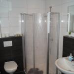 Badezimmer mit Dusche, Waschbecken und Toilette. Weiße Fliesen und dunkle Bodenfliesen.