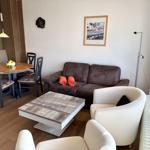 Wohn- und Essbereich mit Sofa, Stühlen und Tisch. Fenster, Lampe und Wandbild sichtbar.