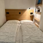 Zwei Betten mit weißen Bettdecken und Holz-Kopfteil. An der Wand hängen Bücherregale.